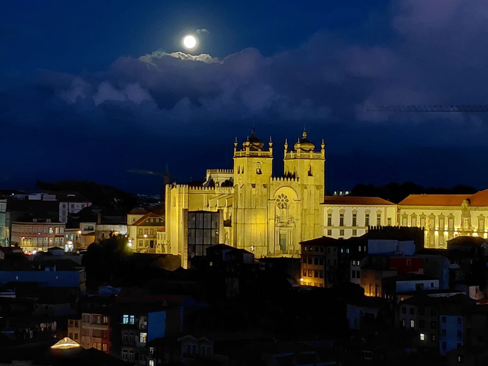 Night view of Porto's illuminated Sé Cathedral, with the full moon rising between clouds